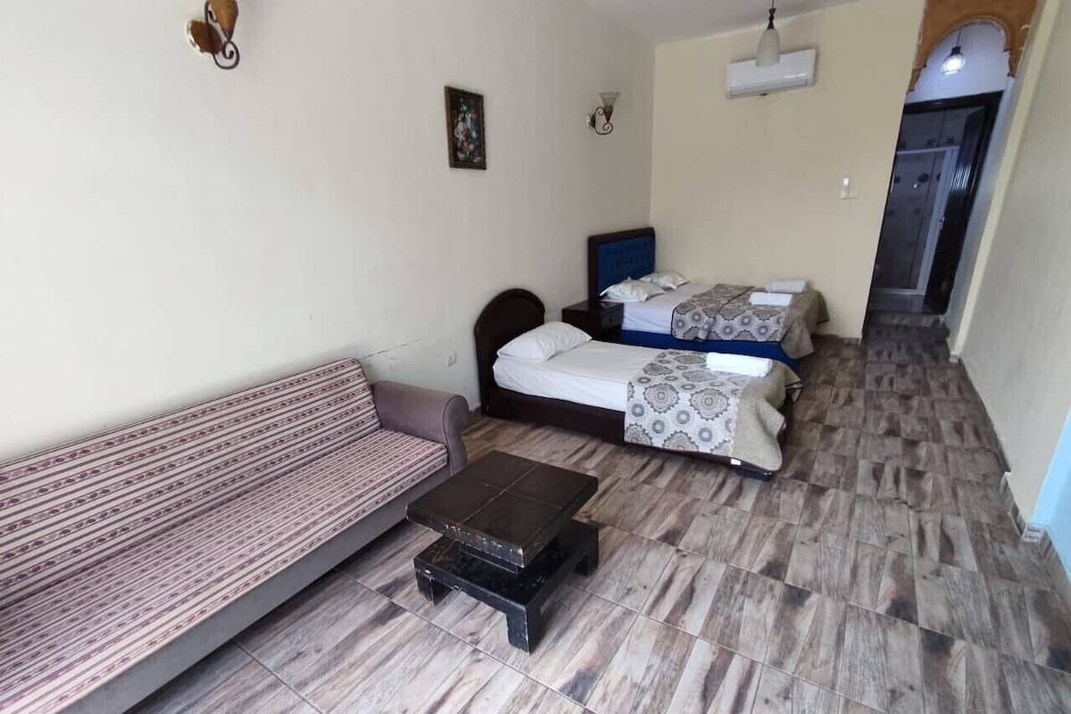 Una habitación pequeña amoblada con sofá, dos camas, una mesita y aire acondicionado instalado en la pared.