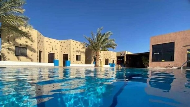 A swimming pool with clear blue water, surrounded by palm trees and a building with a patterned facade. - Bait Alaqaba Resort and Dive Center (Aqaba)