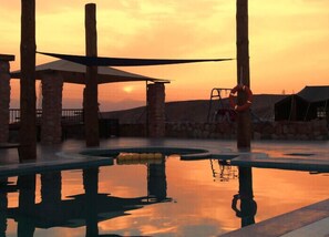 Une piscine avec vue sur le coucher de soleil, entourée de piliers en pierre et agrémentée d’une bouée de sauvetage.