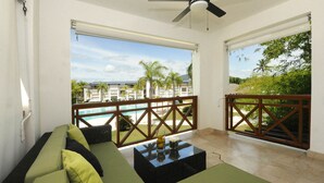 Un balcone con vista su piscina e palme, un divano e un tavolo con un bicchiere d'acqua.