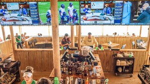 A bar area with multiple screens displaying sports events, wooden furniture, and a variety of bottles and glasses on the bar counter. - Bayshore Beach House - Walk to Nokomis Beach!  Close to Siesta Key, Venice Beach (Nokomis)