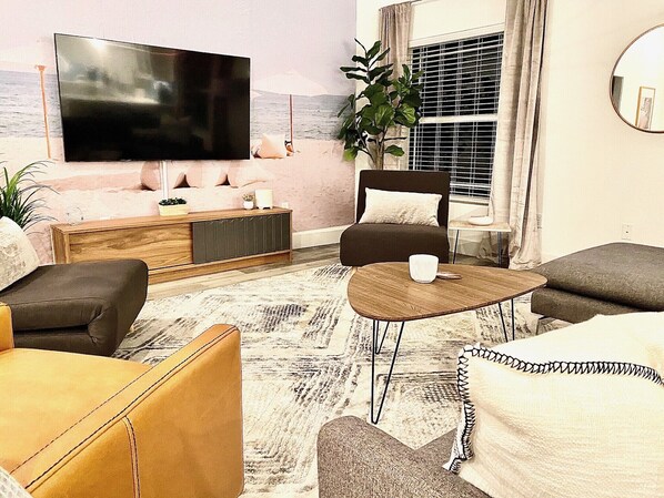 A living room with a flat-screen TV, a sofa, a coffee table, and a potted plant. - Bayshore Beach House - Walk to Nokomis Beach! Close to Siesta Key, Venice Beach (Nokomis)