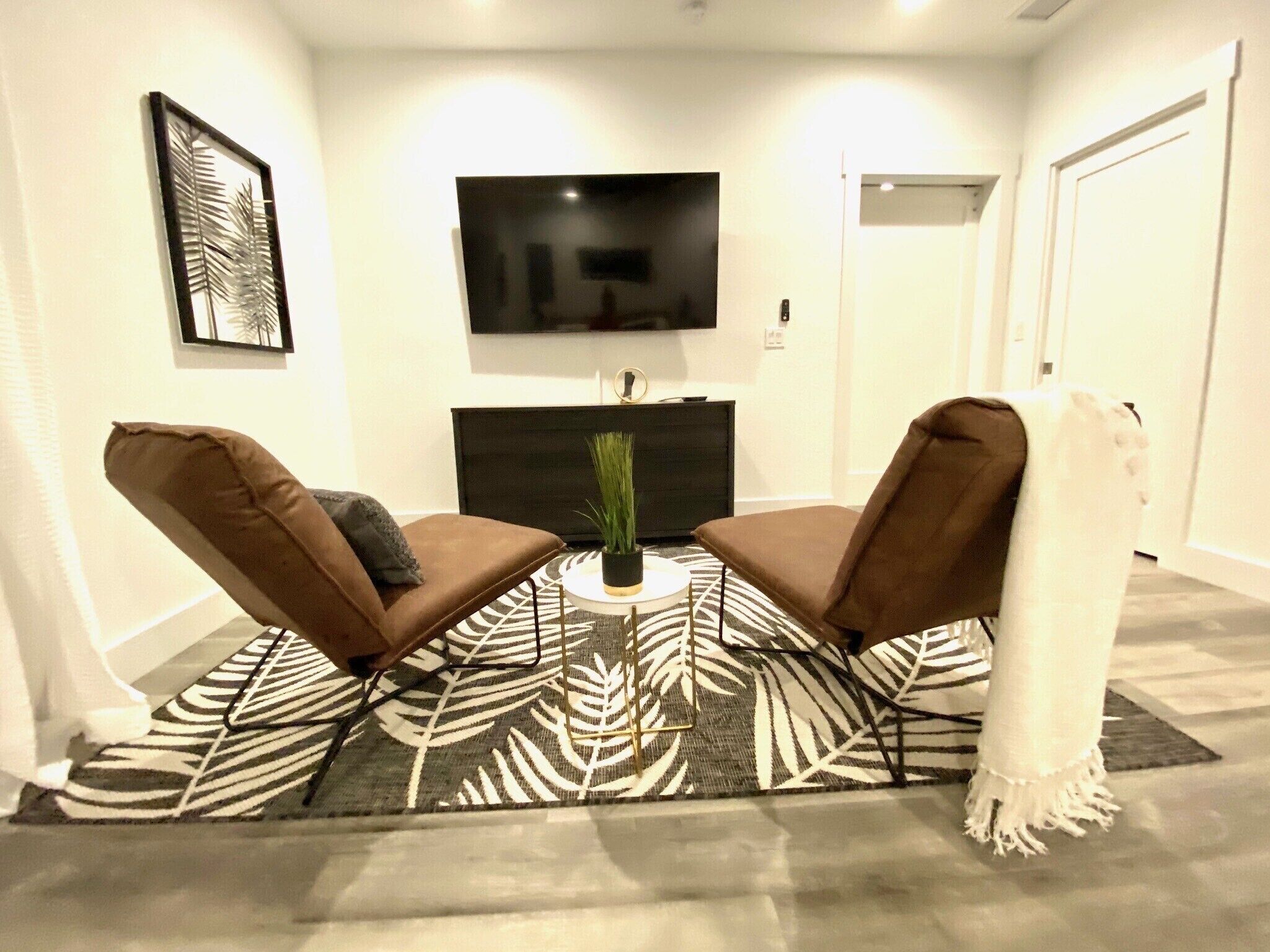 A modern living room with two brown leather armchairs, a black entertainment unit, a flat-screen TV, and a patterned rug.