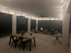 An outdoor patio with a wooden table and chairs, string lights, and a ceiling fan. - Bayshore Beach House - Walk to Nokomis Beach!  Close to Siesta Key, Venice Beach (Nokomis)