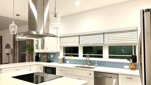 A modern kitchen with white cabinetry, a stainless steel dishwasher, a built-in oven, and a window with blinds. - Bayshore Beach House - Walk to Nokomis Beach!  Close to Siesta Key, Venice Beach (Nokomis)