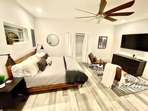 A modern bedroom with a bed, a desk, a chair, a TV, and a ceiling fan. - Bayshore Beach House - Walk to Nokomis Beach!  Close to Siesta Key, Venice Beach (Nokomis)