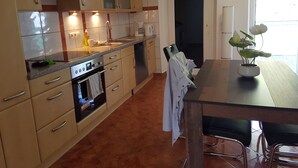 Eine moderne Küche mit Edelstahlgeräten, ein Essbereich mit Tisch und Stühlen und ein Blick durch eine Glastür.