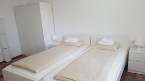 Ein Doppelbett mit beiger Decke und Kissen, ein Nachttisch mit Lampe und ein Kleiderschrank.