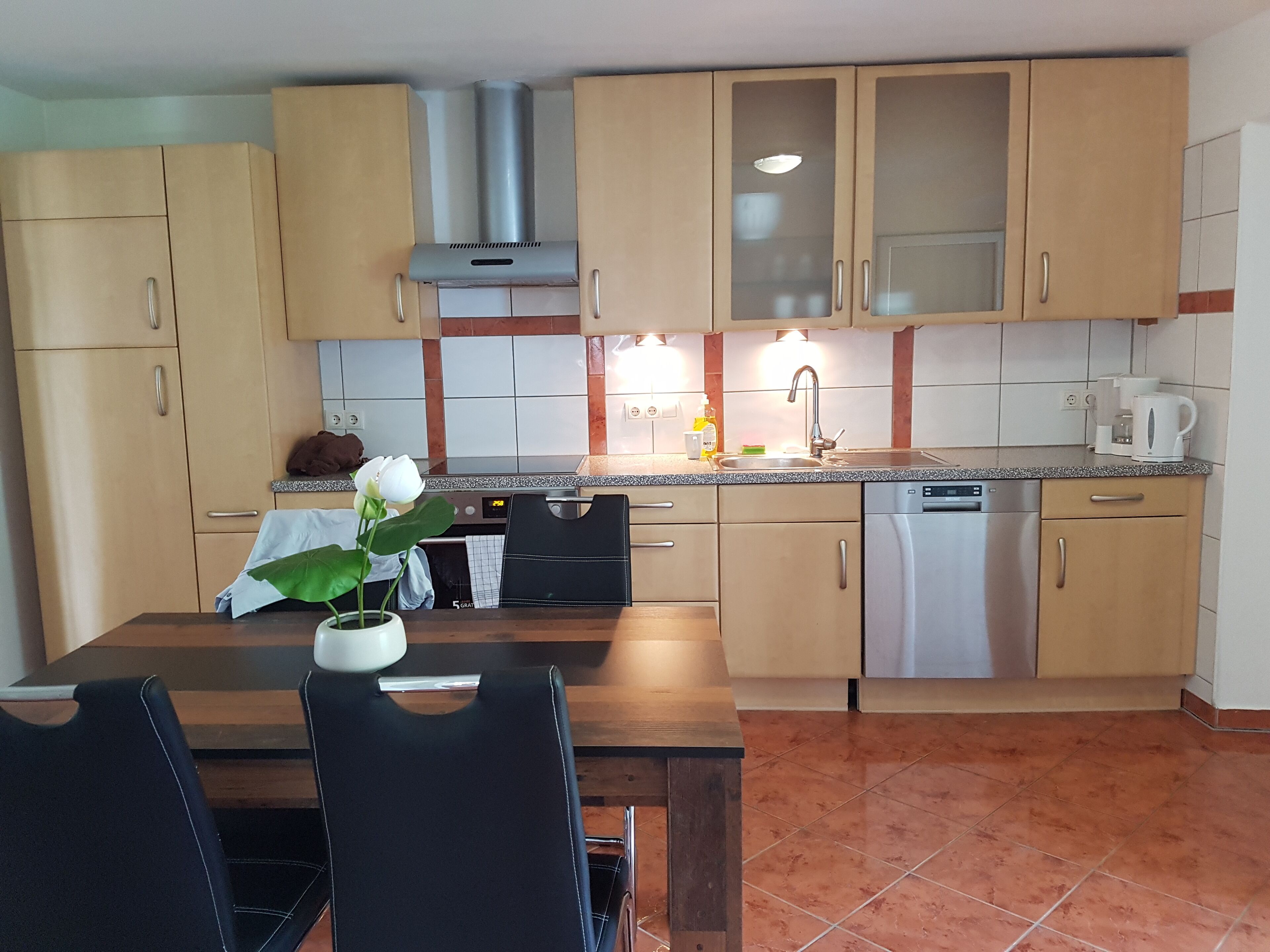 A modern kitchen with wooden cabinets, a stainless steel dishwasher, and a dining area with a table and chairs.