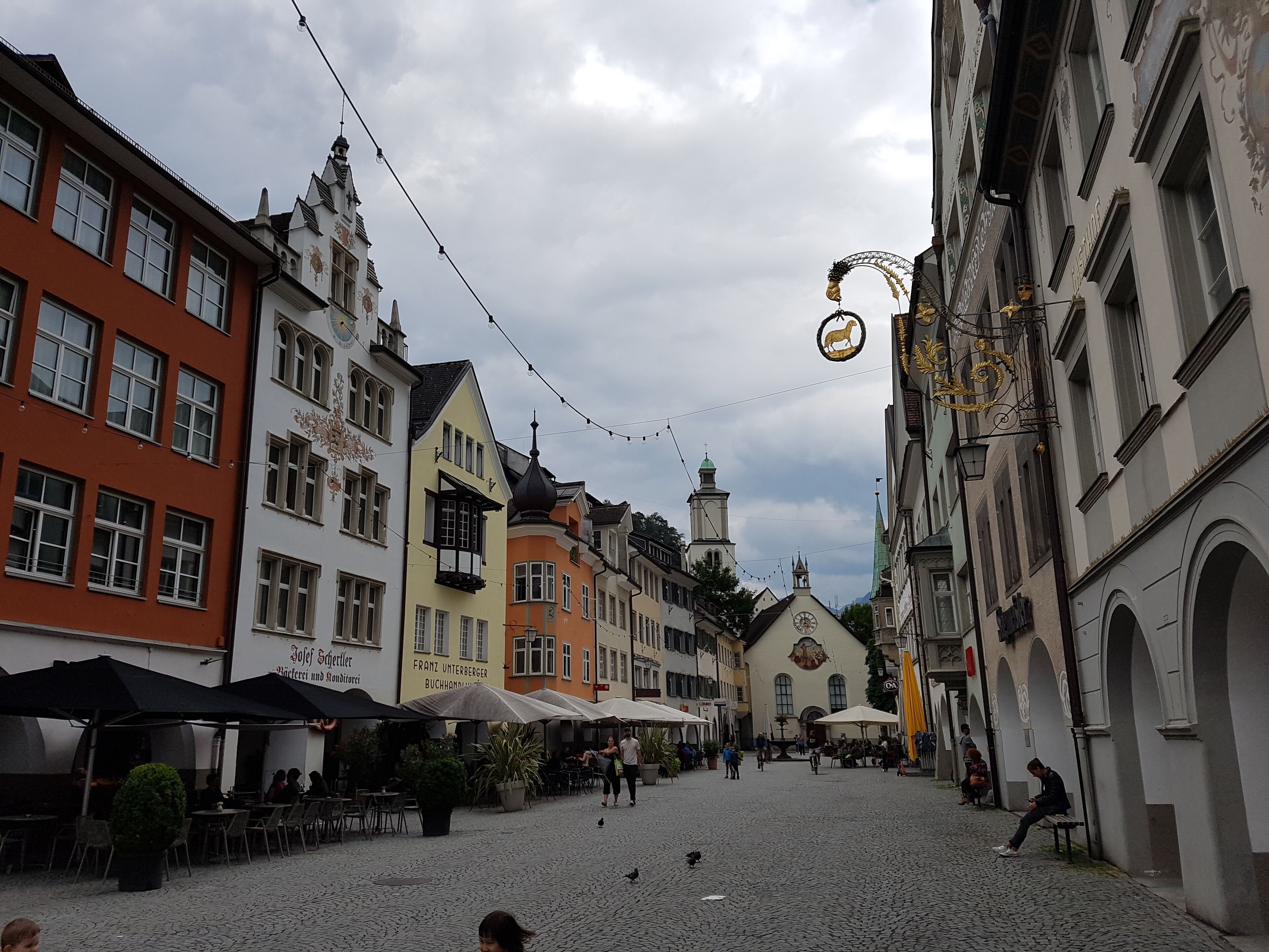 Ein Kopfsteinpflasterplatz mit historischen Gebäuden, Außenbestuhlung und einer Kirche mit einem Kirchturm.