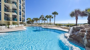 A swimming pool with lounge chairs, palm trees, and a building with balconies. - Great beachfront condo!  Best View in Destin! Jade East Towers unit 920! (Destin)