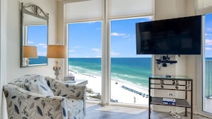 A room with a large window overlooking a beach, a television, a chair, and a small table. - Great beachfront condo!  Best View in Destin! Jade East Towers unit 920! (Destin)