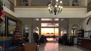 A spacious lobby with a large Christmas tree, seating area, and a view of a sunset through large windows. - Resorto Condominio frente al mar directamente en el océano - Vista marina (Marina Mazatlán)