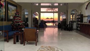 A spacious lobby with a large Christmas tree, seating area, and a view of a sunset through large windows.