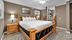 A bedroom with a wooden bed, two bedside tables, a ceiling fan, and a framed picture on the wall. - Eureka Uptown Garden Cottage (Eureka Springs)