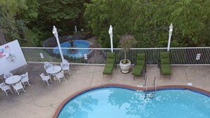A swimming pool with a brick border, surrounded by green lounge chairs and white tables. - Eureka Uptown Garden Cottage (Eureka Springs)
