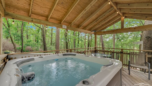 A hot tub area with a wooden deck, surrounded by trees. - Eureka Uptown Garden Cottage (Eureka Springs)