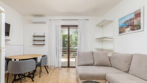 Una sala moderna con una mesa de comedor de madera, sillas grises, un sofá beige y una mesa de centro negra. Hay un ventanal corredero que da a un balcón con vistas a zonas verdes.
