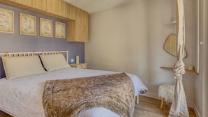 A bedroom with a bed, wooden headboard, a canopy, and framed artwork on the wall.
