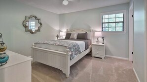 Quarto com cama, mesas de cabeceira, cômoda, espelho e janela.