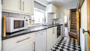 Cucina con mobili bianchi, microonde, lavastoviglie e pavimento a scacchi.