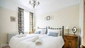 Camera da letto con un letto matrimoniale, un termosifone, un comodino in legno con una lampada e un lampadario.