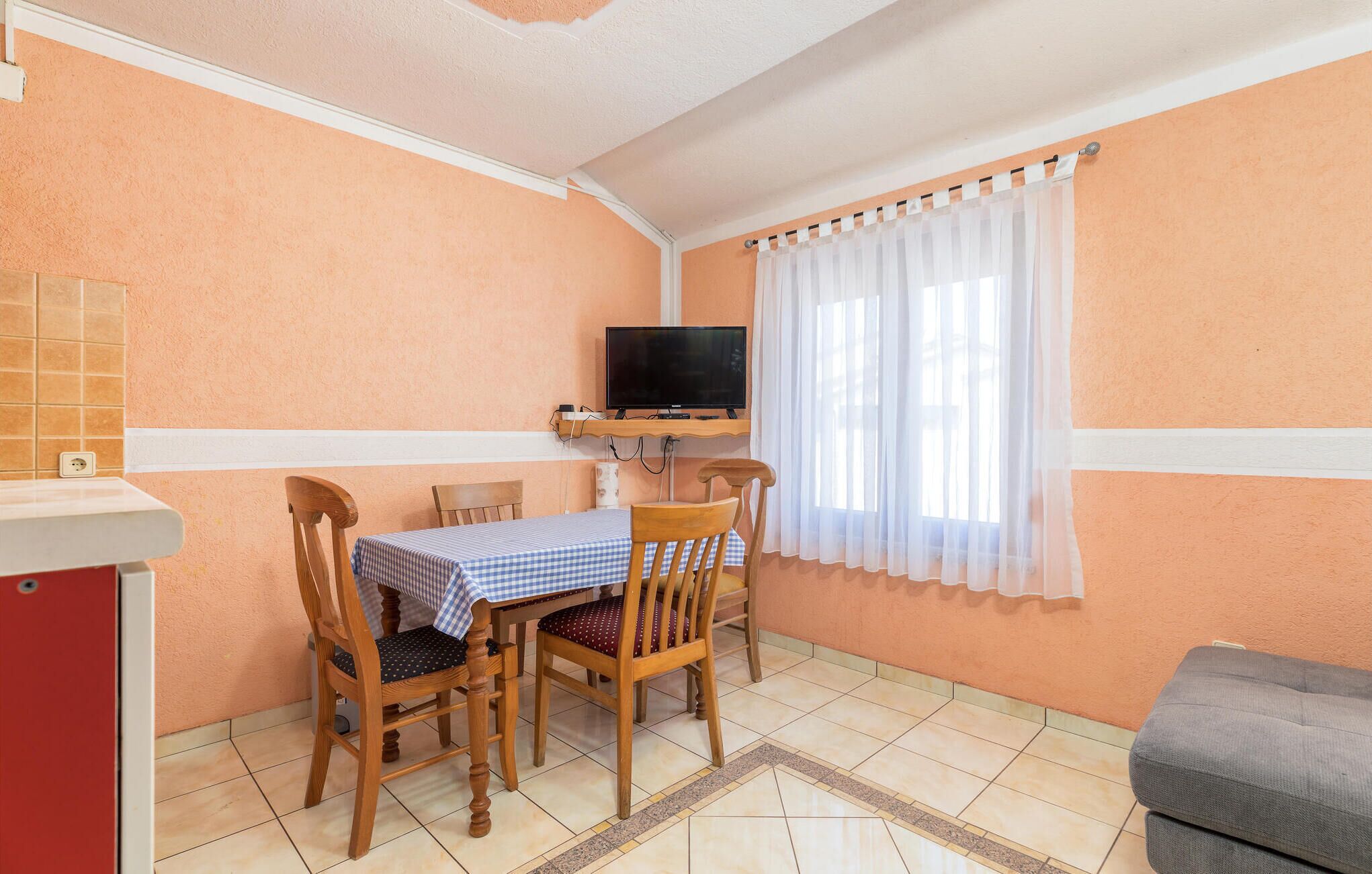 A small room with a dining table, chairs, a television, and a window with curtains.