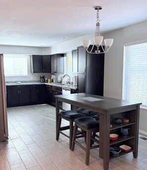 A modern kitchen with dark cabinets, a central island with stools, and a pendant light.
