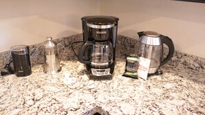 Een aanrecht met een koffiezetapparaat, waterkoker, thermosfles en koffiecups.