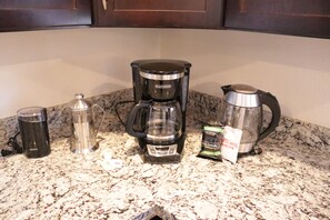 Una encimera de cocina con una cafetera, un hervidor, una termo y cápsulas de café.