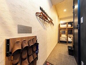 Een hotelgang met een welkomstbord, een schoenenrek, stapelbedden en een deur.