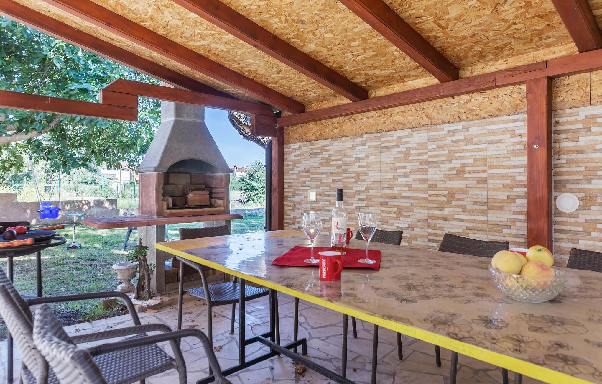 Een terras buiten met een bakstenen muur, een houten plafond en een pizzaoven.