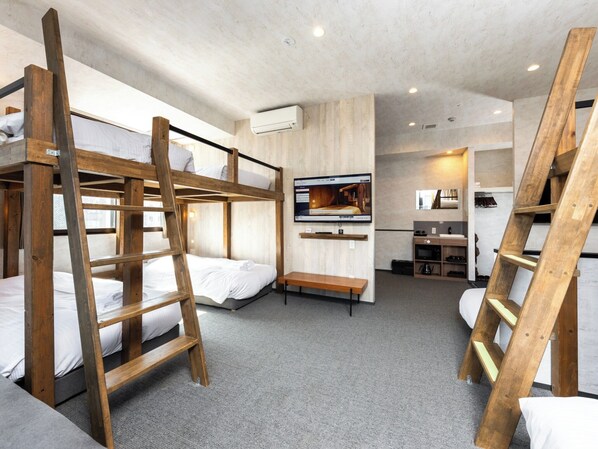 Een slaapkamer met stapelbed, televisie, houten trap en een kitchenette.