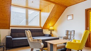Een gezellige woonkamer met een schuine kap, een bank, twee stoelen, een bijzettafeltje en een lamp.
