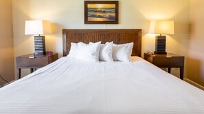 A neatly made bed with white linens, two bedside tables with lamps, a wooden headboard, and a framed picture on the wall. - Waikiki | Waikiki Sunset Stay | Pool & Hot Tub (Honolulu, Ohau)