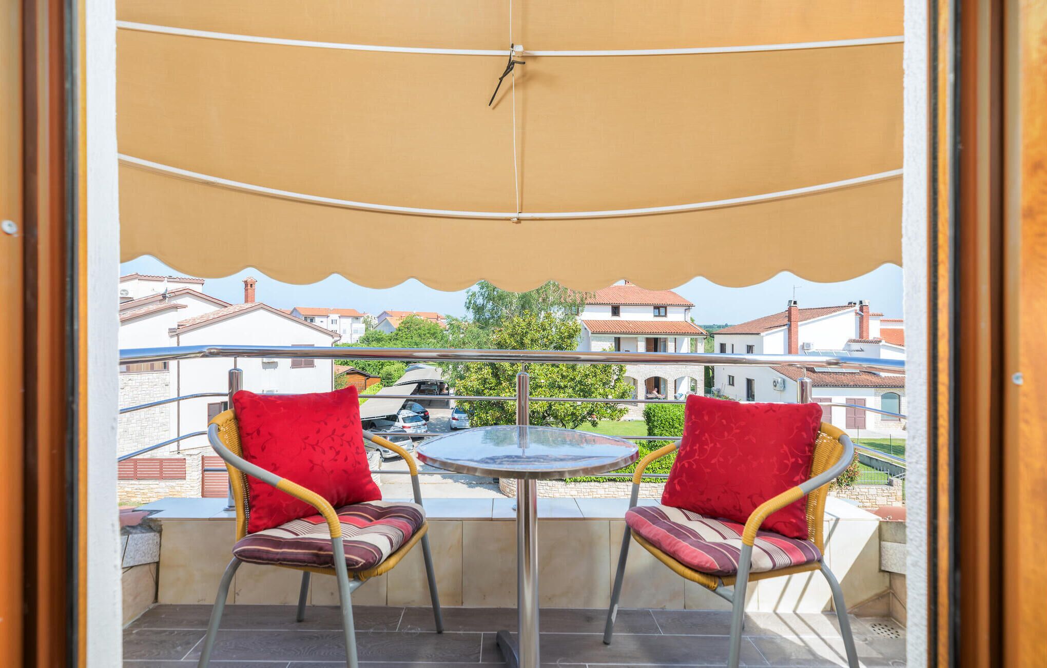 Een balkon met twee rieten stoelen, een klein rond tafeltje en een beige zonnescherm.