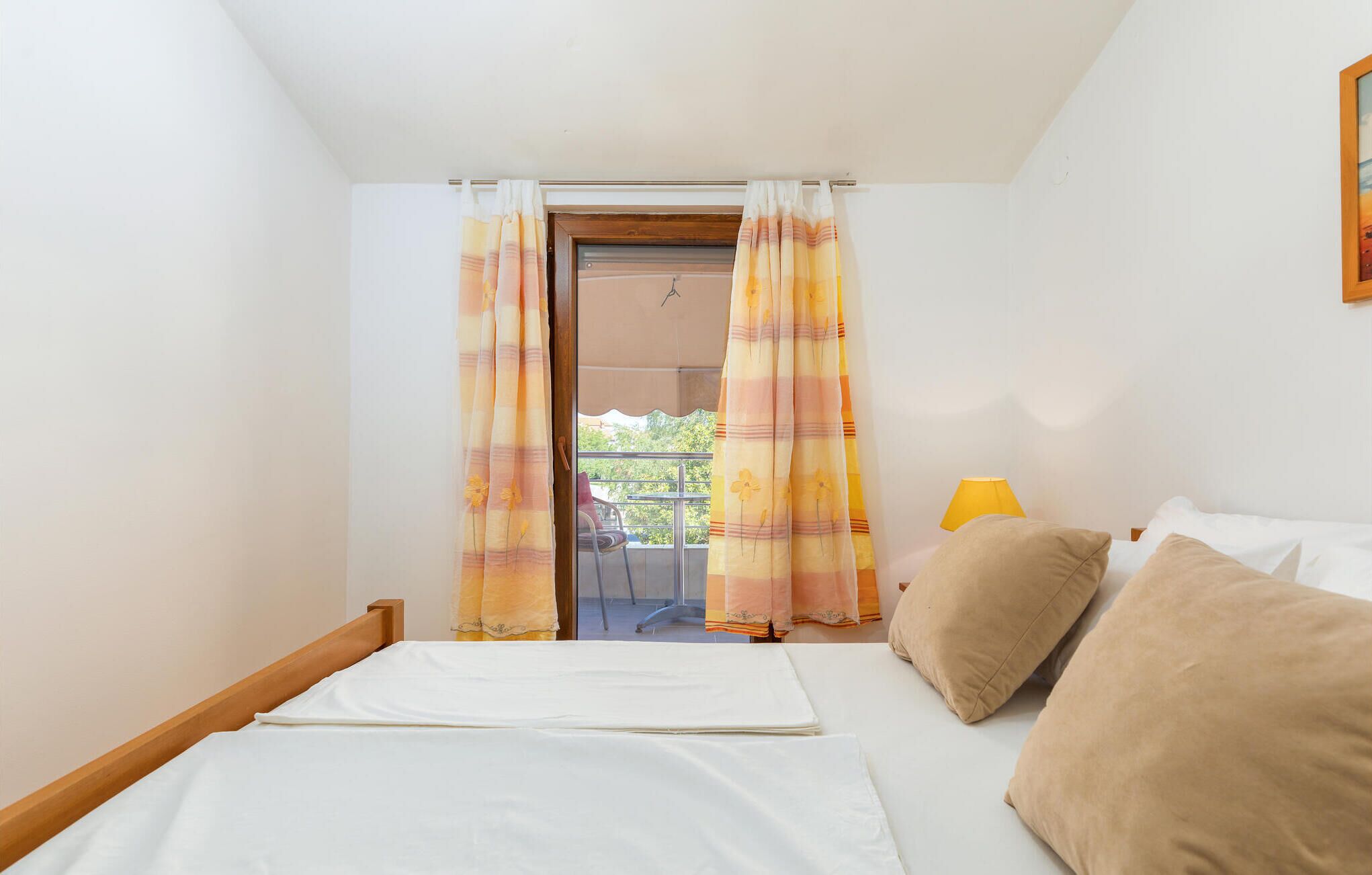 Een slaapkamer met een bed, twee kussens, een nachtkastje met een lamp en een raam met gordijnen.