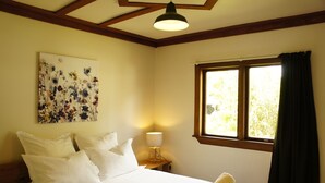 A neatly made bed with white linens, a bedside lamp, and a window with curtains. - Welcome Home Cottage, Manapouri, Fiordland (Manapouri)