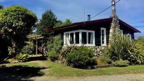 A stone house with a red roof, white windows, and a stone chimney. - Welcome Home Cottage, Manapouri, Fiordland (Manapouri)