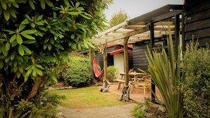 A garden with a wooden pergola, a hammock, and a table with chairs. - Welcome Home Cottage, Manapouri, Fiordland (Manapouri)