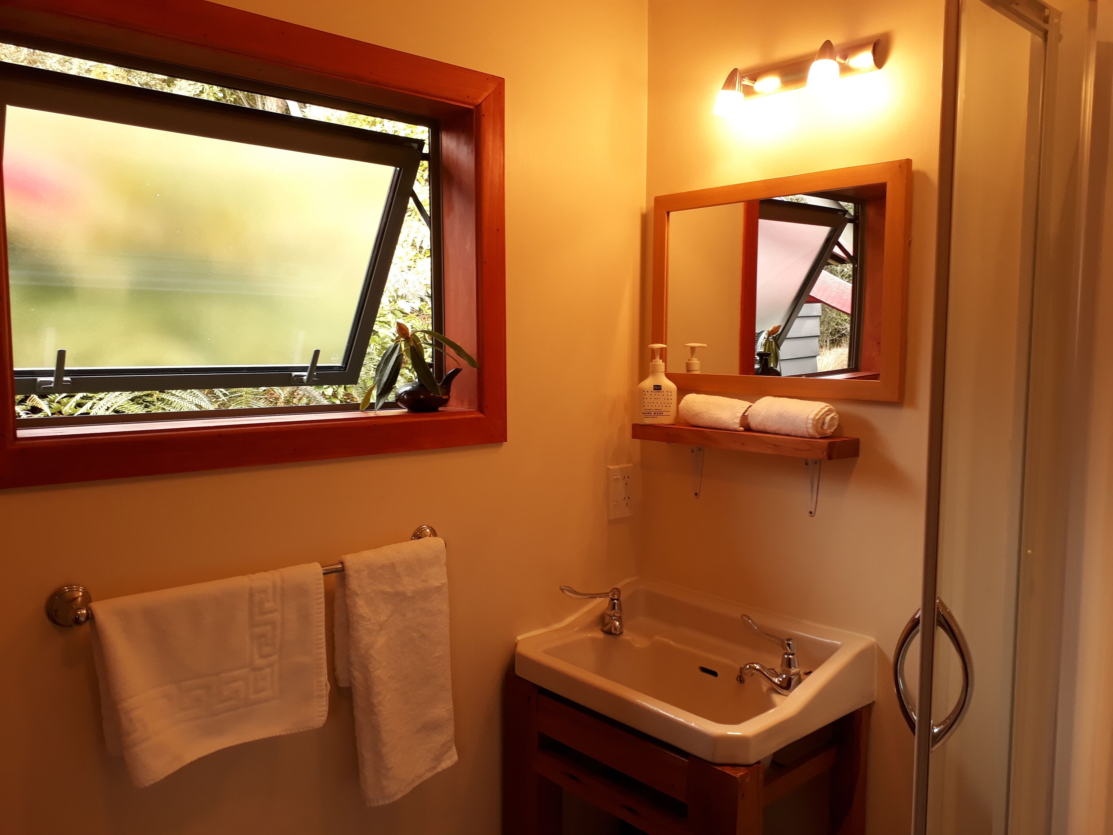 Un baño con ventana, lavamanos, espejo y un perchero para toallas.