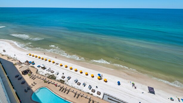 Eine Vogelperspektive zeigt einen Strand mit Pool, Sonnenschirmen und Liegestühlen.