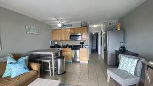 A modern kitchen with wooden cabinets, a microwave, and a refrigerator. There is a dining area with a table and chairs, and a living room with a sofa and a coffee table. - Beautiful Ocean View/ Steps to Beach and Pool (Hilton Head Island)