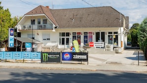 A two-story building with a tiled roof, a balcony on the upper floor, and multiple signs including Pepsi and Balaton ABC. - Familia 2 by Interhome (Balatonszemes)