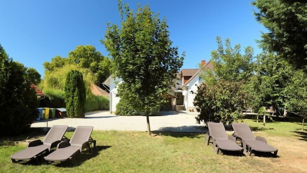 A backyard with two rows of sun loungers, a tree, and a house in the background. - Familia 2 by Interhome (Balatonszemes)