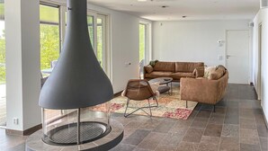 Una sala de estar moderna con una chimenea grande, un sofá de cuero marrón, un sillón de mimbre y una alfombra estampada.