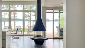 Un interior moderno con un ventanal grande que da a un lago, una lámpara azul central y una zona de comedor con sillas.