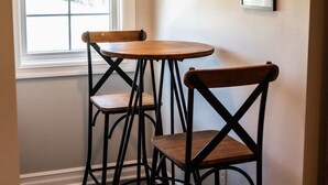 A corner with two wooden tables and chairs, a window with blinds, and a framed picture on the wall.