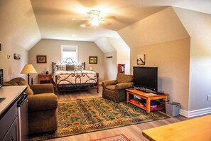 An attic bedroom with a bed, a television, a chair, a lamp, and a ceiling fan. - Studio near Kettle Moraine Forest-hikers paradise! (Kewaskum)