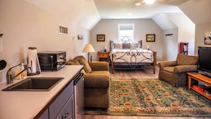 A compact room with a kitchenette, a bed, a chair, a television, and a ceiling fan.
